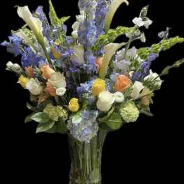 Tall mixed bouquet of blue and white flowers in a clear glass vase