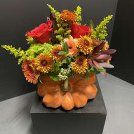 Autumn floral arrangement in a pumpkin-shaped container with red roses and orange blooms
