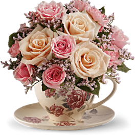 Pink and cream roses arranged in a floral teacup on a saucer