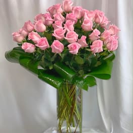 Pink roses arranged in a tall clear glass vase with broad green leaves