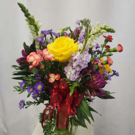 Mixed bouquet with a yellow rose in a glass vase and red ribbon