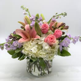 Pink roses and lilies in a clear glass vase with white hydrangeas
