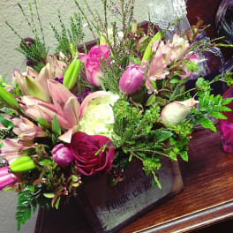 Mixed bouquet of pink lilies, roses, and tulips in a rustic container