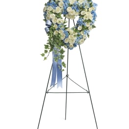 Heart-shaped floral wreath on a stand with white roses and blue flowers