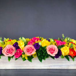 Long rectangular flower arrangement with pink, yellow, purple, and orange blooms in a white box