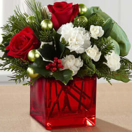 Red roses and white carnations in a red glass vase with holiday ornaments
