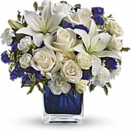 White lilies and roses with blue accents in a square glass vase
