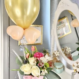 Bouquet of cream and pink flowers in a white vase with gold and peach balloons