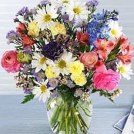 Mixed bouquet of daisies, roses, and colorful blooms in a glass vase