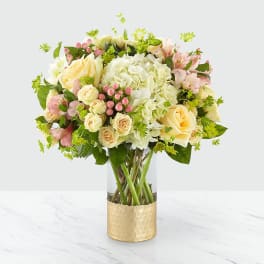 Bouquet of cream and pink flowers in a clear vase with a gold wrap
