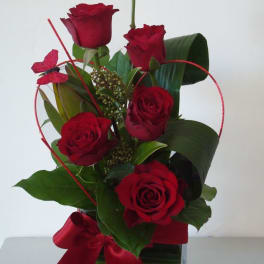 Red roses arranged in a clear square vase with a red ribbon