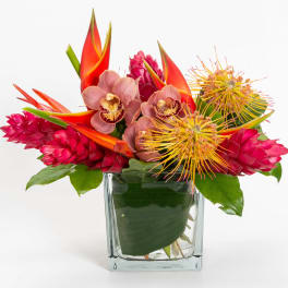 Tropical bouquet in a clear glass vase with pink orchids and red-orange blooms