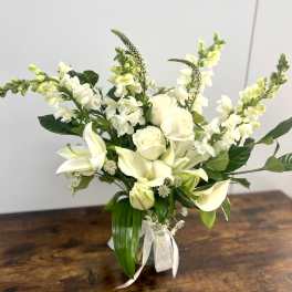 White floral arrangement with roses, calla lilies, and snapdragons in a clear vase