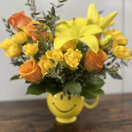 Yellow and orange flower arrangement in a smiley-face mug