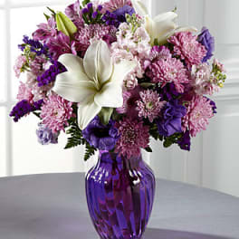 Purple and pink bouquet with white lilies in a purple glass vase
