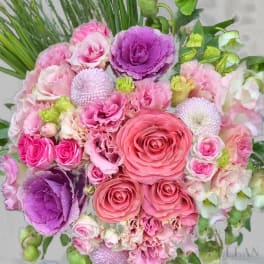 Tightly clustered bouquet of pink roses, ruffled blooms, and purple ornamental cabbages.