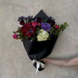 Hand-tied bouquet of pink, purple, red, and white flowers wrapped in black paper
