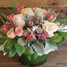 Low arrangement of pink and cream roses and tulips in a green vase with small pink filler blooms