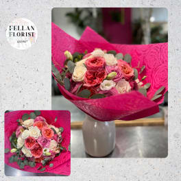 Hand-tied bouquet of pink, peach, and cream roses in bright magenta wrap, displayed in a white vase.