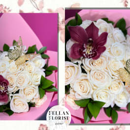 Round bouquet of cream roses with a burgundy orchid and gold butterfly picks in pink wrap.