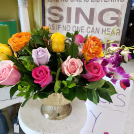 Mixed roses and orchids arranged in a cream pedestal vase