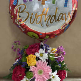 Birthday balloon above a mixed flower arrangement in a decorated cup