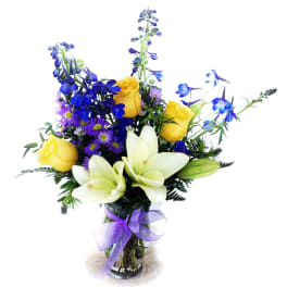 Bouquet of yellow roses, white lilies, and blue flowers in a glass vase