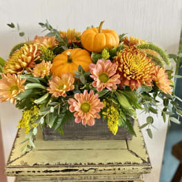 Autumn floral arrangement with orange pumpkins and peach chrysanthemums in a wooden box
