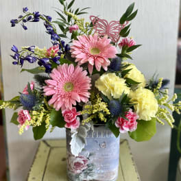 Mixed bouquet in a decorative tin container with pink and yellow flowers