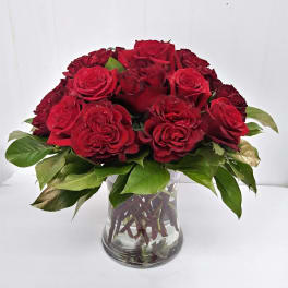 Red roses arranged in a clear glass vase with green leaves