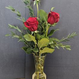 Three red roses in a clear glass vase with greenery