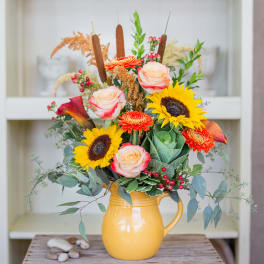 Mixed bouquet in a yellow pitcher with sunflowers, roses, and orange blooms