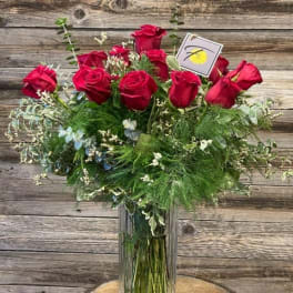 Red roses arranged in a tall glass vase with mixed greenery