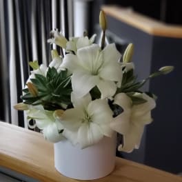 White lilies arranged in a white cylindrical vase