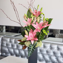 Pink lilies arranged in a tall black vase with branches