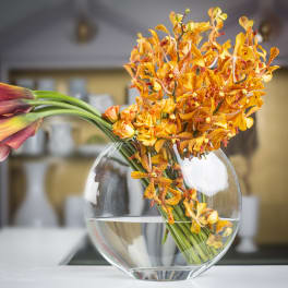 Orange orchids and calla lilies in a round glass vase