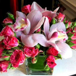 Pink roses and pale lilies arranged in a square glass vase