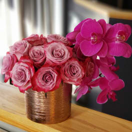Pink roses and magenta orchids arranged in a gold vase