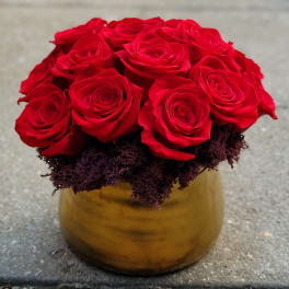 Red roses arranged in a gold vase with dark filler at the base