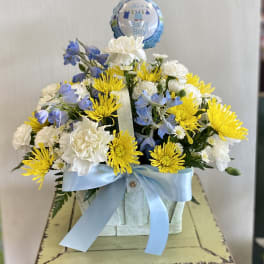 Blue and white flower arrangement in a basket with a baby boy balloon