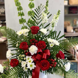 Red roses and white flowers in a white vase with a red ribbon