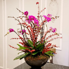 Pink orchids arranged in a dark bowl with red branches and broad green leaves