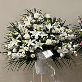 White lilies and roses in a standing spray with a ribboned easel