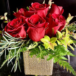 Low arrangement of red roses with foliage in a gold beaded cube vase