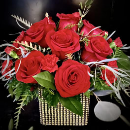 Arrangement of red roses and small red flowers in a gold beaded cube vase