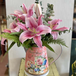 Pink lilies arranged in a decorative metal pitcher with greenery