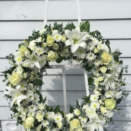 White floral wreath with roses, lilies, and daisies on a stand