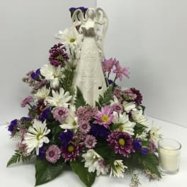 White angel figurine surrounded by purple, pink, and white flowers with a candle nearby