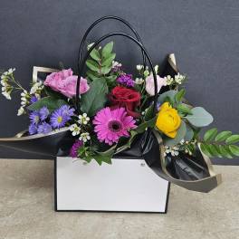 Mixed bouquet in a black handled gift bag with pink, red, yellow, and purple flowers