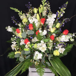 Large mixed floral arrangement with red and yellow roses in a white crate